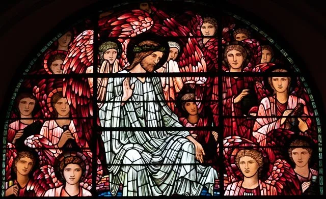 Colorful stained glass window depicting Jesus Christ with angels around him and red wings behind him.
