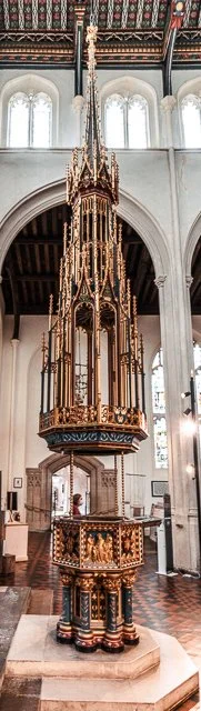 A tall, ornate wooden pulpit inside a church with high arched windows and decorative details.