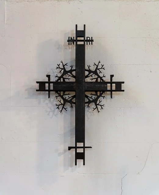 Decorative black metal wall art with a cross shape and snowflake design on a white brick wall.