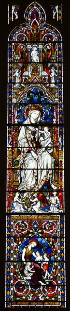 Stained glass church window depicting a seated female figure with a crown, surrounded by angels and religious symbols, with intricate patterns and vibrant colors.