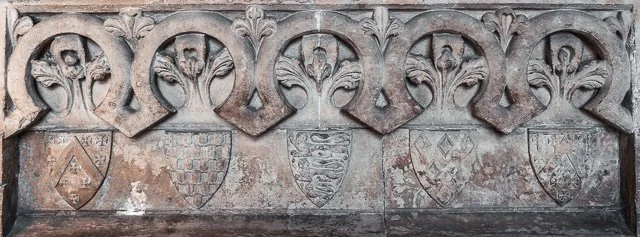 Stone wall with decorative carved elements and heraldic shields.