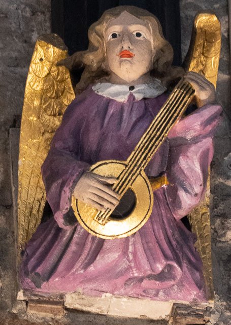 Painted wooden statue of an angel playing a guitar, with gold wings and pink robes.