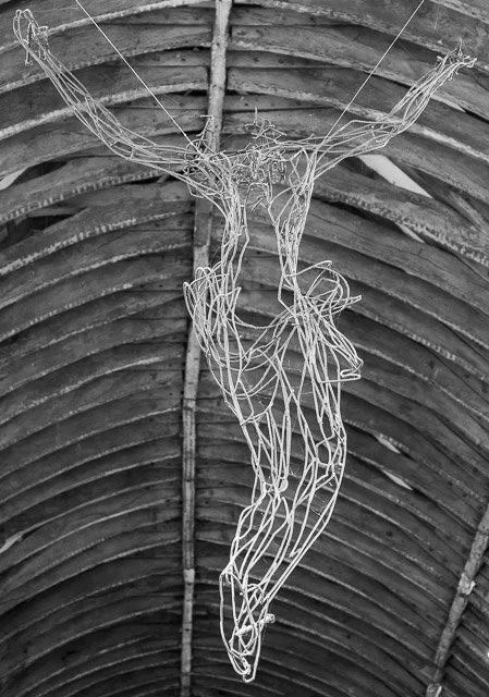 Wire sculpture of Jesus on the cross hanging inside a barn or wooden structure.