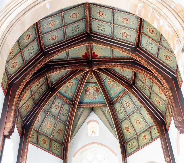 Ornate painted ceiling in a historic building with floral and geometric designs and a small window underneath.