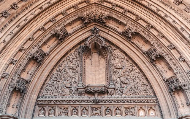 Close-up of an ornate, carved stone archway on a historic building, featuring detailed biblical and religious relief sculptures.