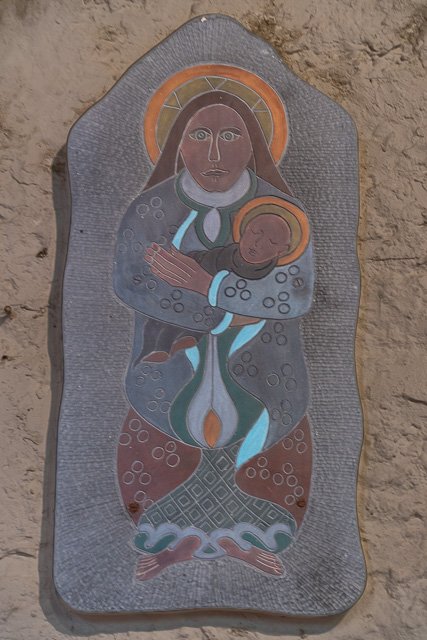 Religious wall art depicting a figure of a woman holding a child, with a halo around her head, on a textured stone background.