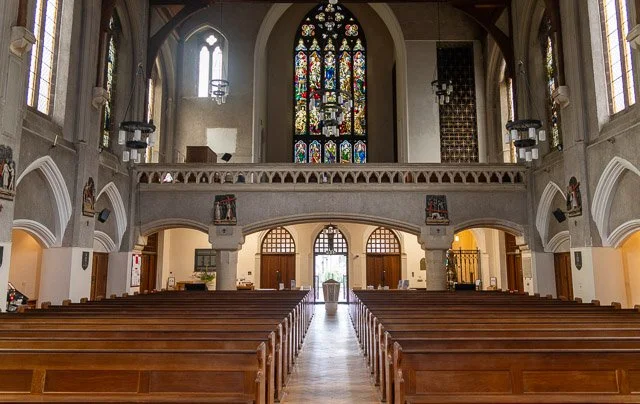 Interior of a church with wooden pews, stained glass windows, and an altar at the front.