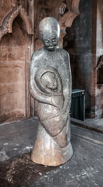 Stone sculpture of a human figure holding a circular object in front of the body, set in a wooden and stone interior