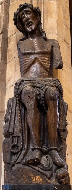 Wooden sculpture of Jesus Christ, depicting the suffering and crucifixion, with a crown of thorns on his head, in a church or cathedral setting.