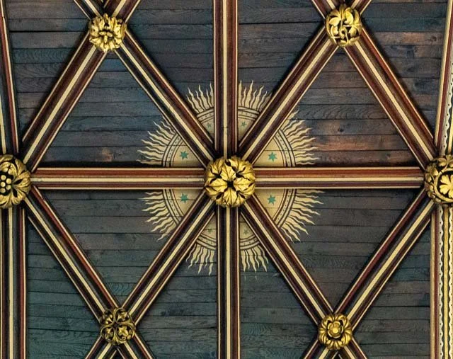 Ceiling with wooden beams and decorative gold accents, featuring a painted sunburst design with a central star and surrounding rays.