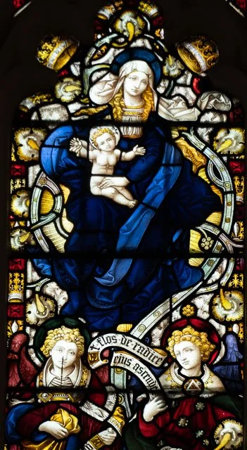 Stained glass window depicting Virgin Mary holding baby Jesus, with angels at her sides.