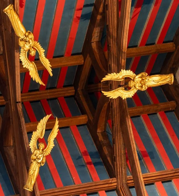 Decorative golden angel and bird ornaments hanging from a wooden ceiling with striped blue, red, and white fabric.