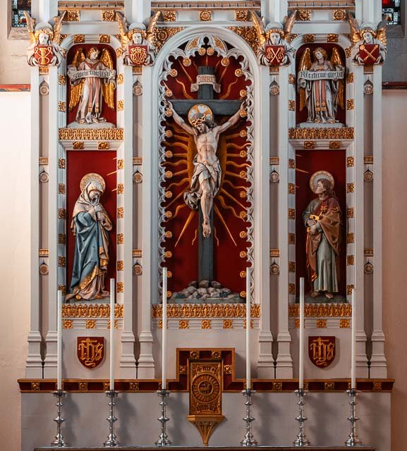 A detailed religious altar with a crucifix in the center, flanked by statues of saints and angels, decorated with gold and red accents.