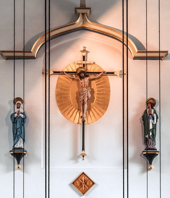 Religious altar with a crucifix of Jesus Christ in the center, flanked by statues of saints, in a church setting.