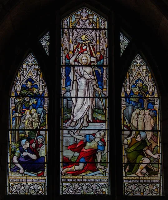 Colorful stained glass window depicting a religious scene with Jesus Christ ascending to heaven, surrounded by angels, and people looking up in awe.