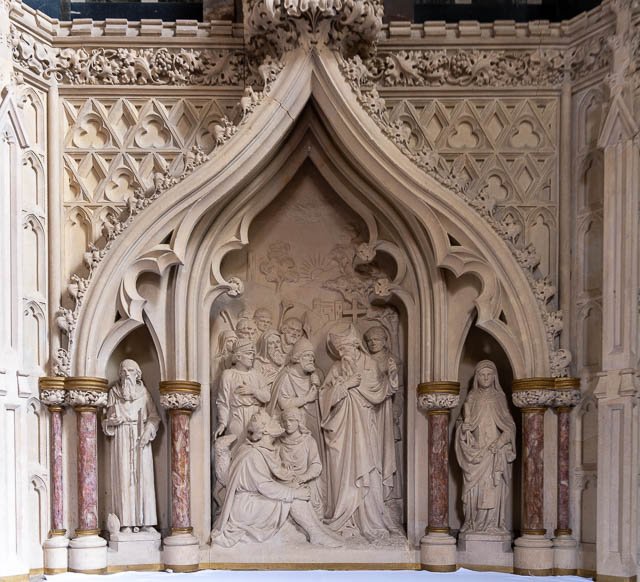 Religious stone sculpture depicting Jesus Christ's crucifixion scene with multiple figures, framed by ornate gothic architectural details.