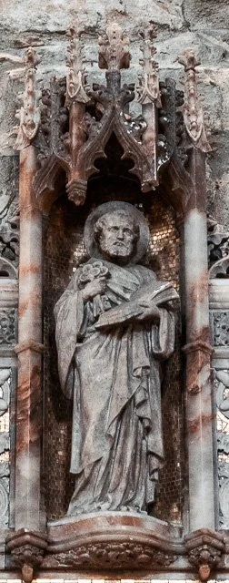 Stone religious sculpture of a bearded man holding a book, set in a decorative architectural niche with ornate carvings and columns.