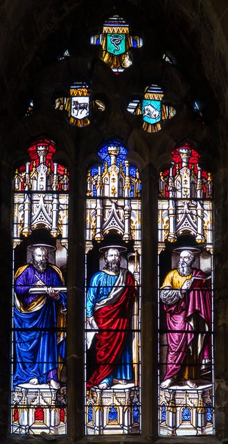Stained glass church window depicting three biblical saints with halos, holding books or scrolls, with blue, red, and purple robes.