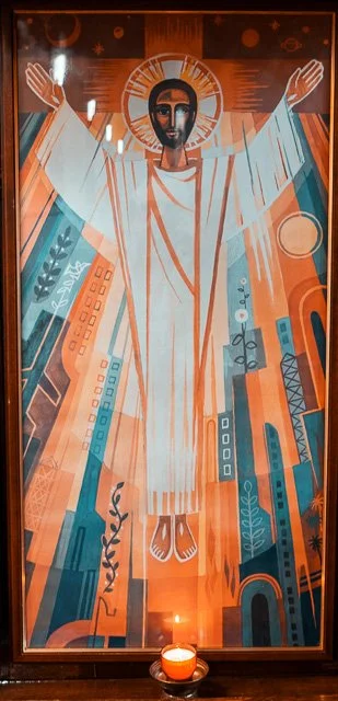 A stylized religious icon of Jesus Christ with outstretched arms, surrounded by a halo, depicted in a modern, geometric art style with orange, blue, and beige colors.