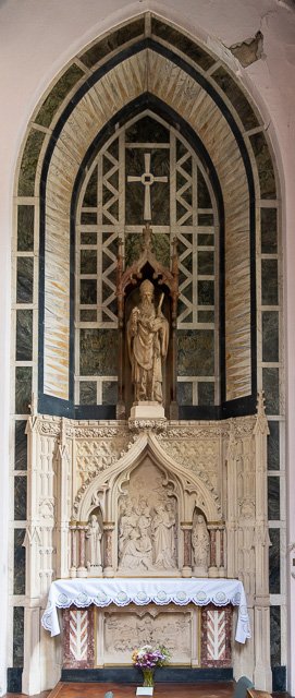 Religious altar with a statue of Jesus Christ, ornate stone carvings, and a white cloth on the altar table with flowers in front.