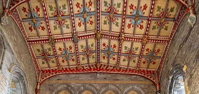 Ceiling with ornate painted and carved decorations, featuring crosses and floral motifs in red, green, blue, and gold, in a historic building.