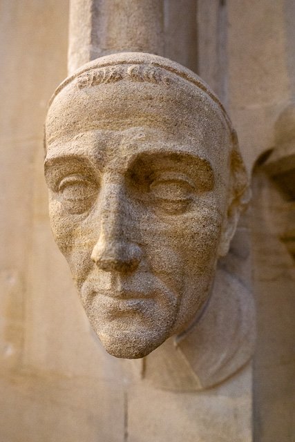 Close-up of a stone sculpture of a man's face, positioned on a wall or building exterior.