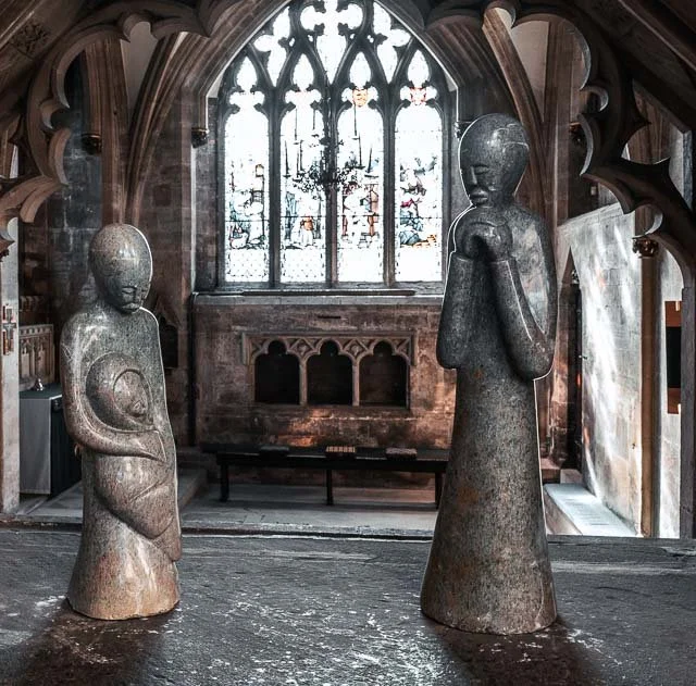 Two stone sculptures of children are inside a church with stained glass windows and Gothic architecture.