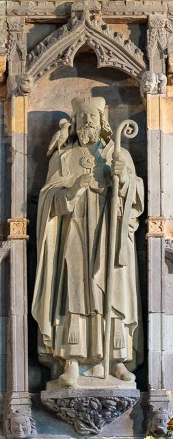 Stone sculpture of a bearded man holding a staff and a scroll, standing on a decorated base within a Gothic-style architectural niche.