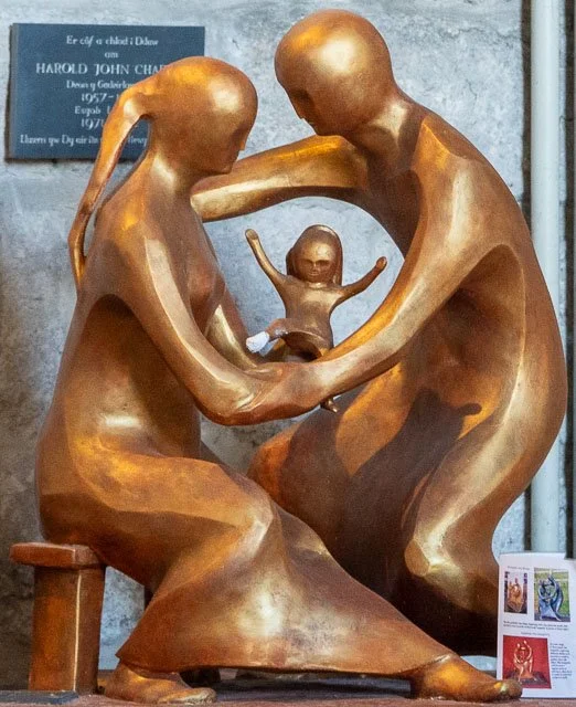 Bronze sculpture of a seated couple holding a small child between them, with a plaque in the background.