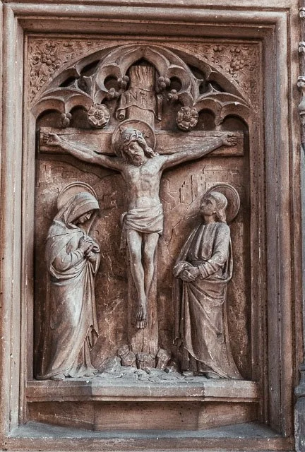 Wooden relief sculpture of the crucifixion of Jesus, with Jesus on the cross flanked by Mary and John the Apostle.