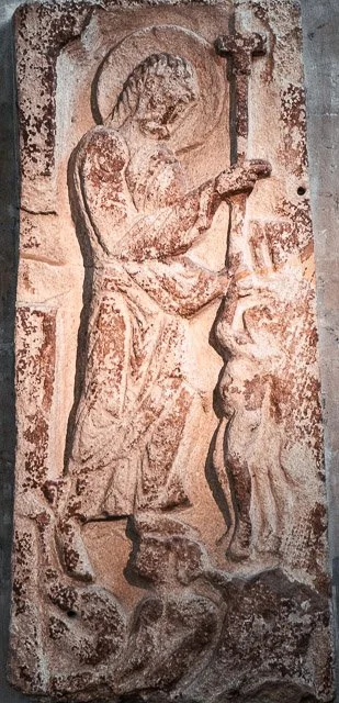 Relief carving of Jesus Christ with a halo, holding a cross, and healing a person.