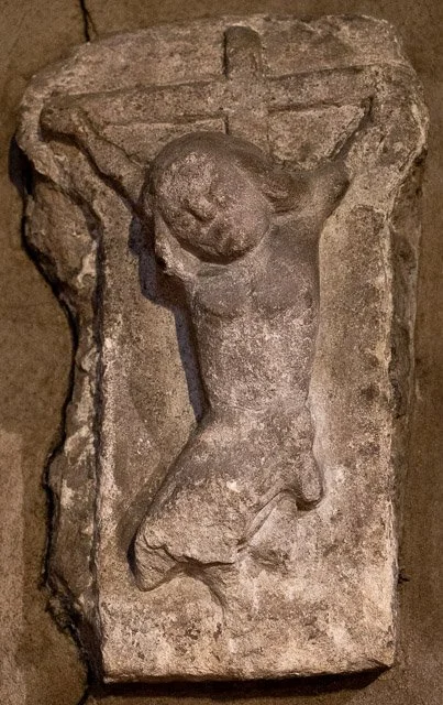 A stone carving depicting Jesus Christ on the cross, with his head bowed and body hanging, showing signs of age and weathering.