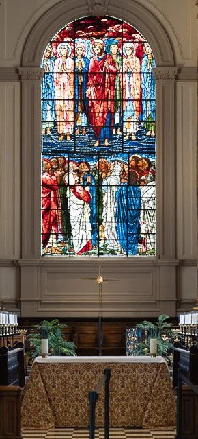 A religious stained glass window depicting Jesus Christ surrounded by angels and saints, with a congregation below, in a church interior.