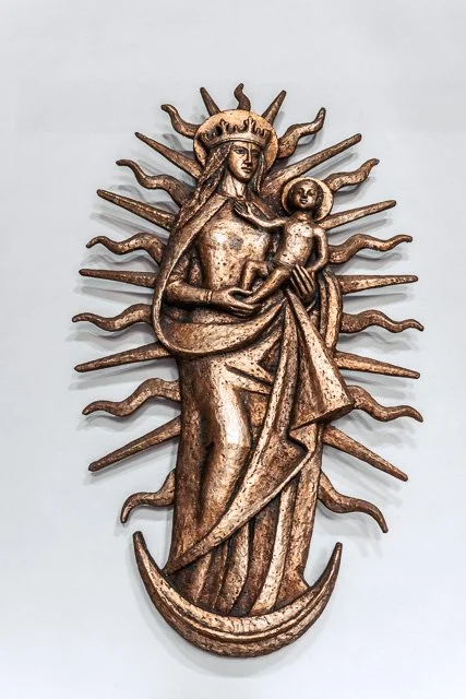 Metal wall sculpture of a woman holding a child, with a sunburst and moon elements in the background.
