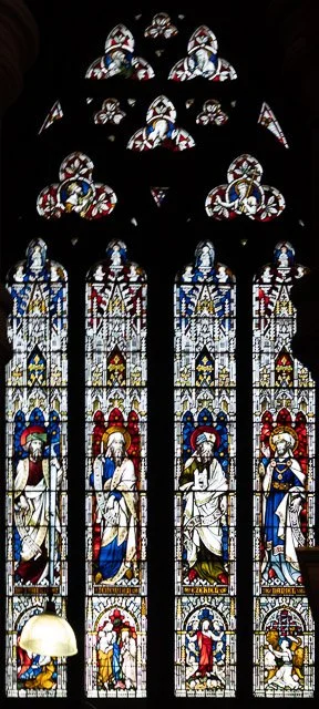 Colorful stained glass windows in a Gothic cathedral with religious figures and intricate designs.