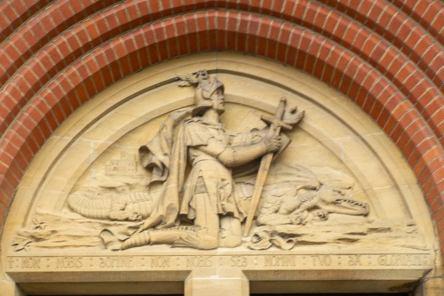 Stone carved relief of a knight with a sword, flanked by crocodiles and a dragon, set in a brick arch.