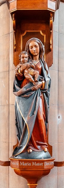 Statue of the Virgin Mary holding baby Jesus in a niche with a wooden canopy above.
