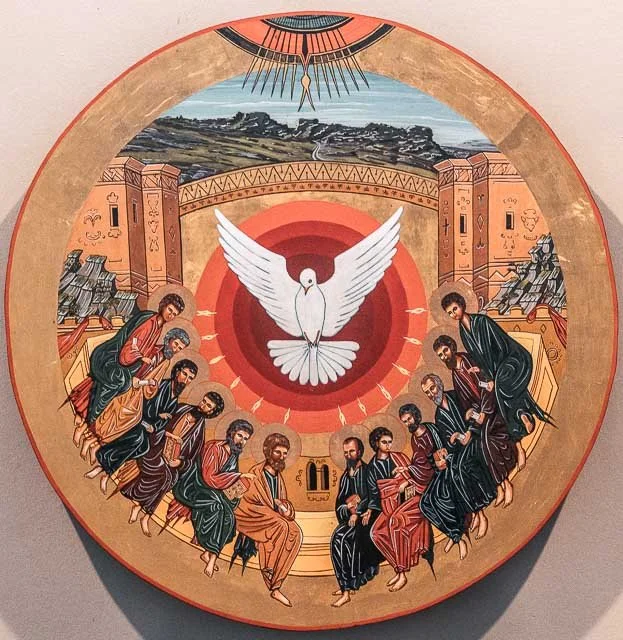 A circular religious icon depicting Jesus and apostles surrounding a white dove at the center, with a landscape scene and architectural elements in the background.