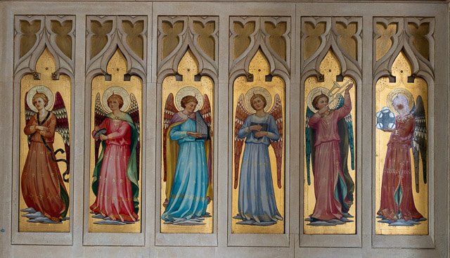 Six painted angel figures with wings and halos, each in different robes, aligned side by side in a church or religious setting.