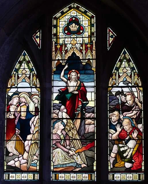 Colorful stained glass window depicting Jesus Christ's resurrection with angels, saints, and biblical figures.
