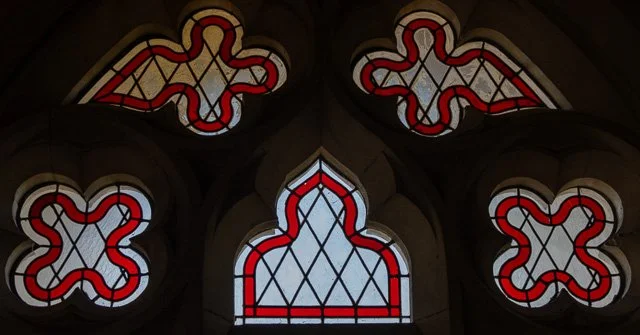 Close-up of stained glass windows with red, white, and blue designs in a Gothic arch shape.