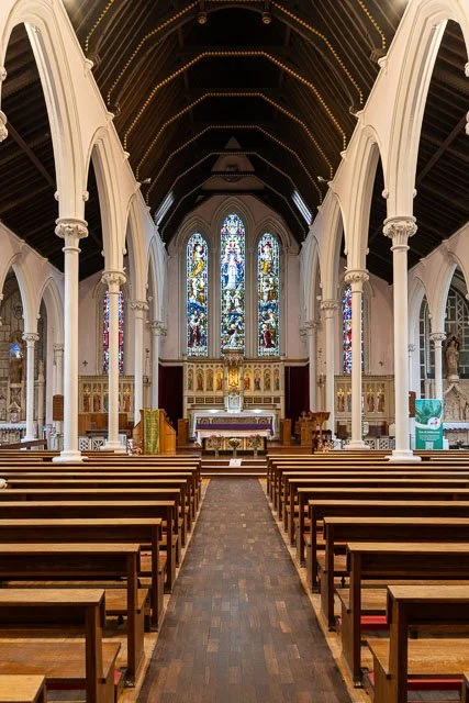 Interior of a church with wooden pews, stained glass windows, and an altar at the front.