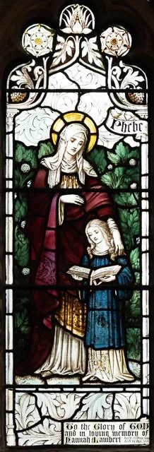 Stained glass window depicting the Virgin Mary holding a book, with a young girl, in front of green trees, with a decorative top and the text 'Penitence'.