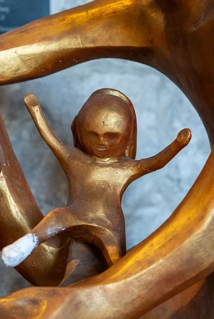 Close-up of a gold-colored sculpture of a person with arms raised, surrounded by abstract swirling shapes.