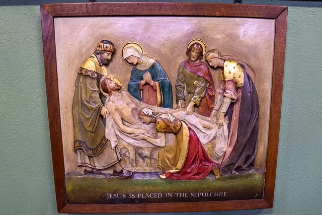 Painting depicting the crucifixion of Jesus, with Jesus lying on a slab surrounded by four women and one man, all in historical clothing. The caption reads, "Jesus is placed in the sepulchre."