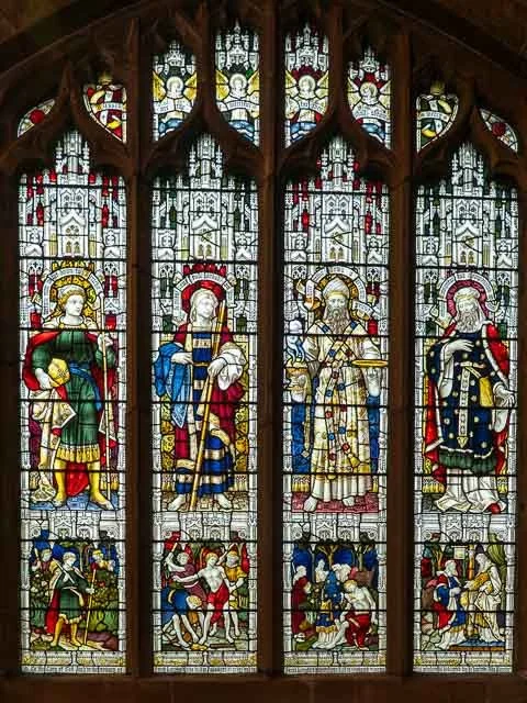 Four stained glass windows depicting religious figures, possibly saints or biblical characters, with scenes below illustrating various activities, all set within an ornate wooden frame.