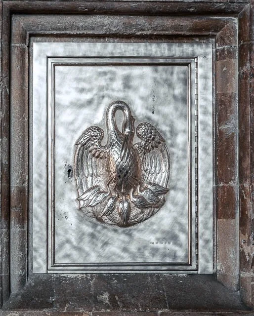Decorative metal door with a raised floral and bird design, set in a brick and wooden frame.