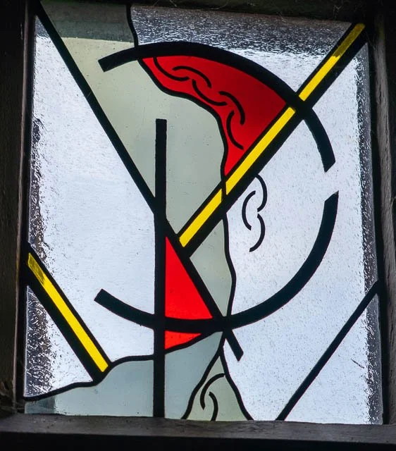 Stained glass window depicting a stylized human profile with a visible brain and face outline, using red, black, gray, and yellow colors.