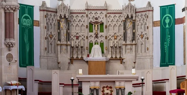 Interior of a church altar with white ornate architecture, green banners on each side, and lit candles.