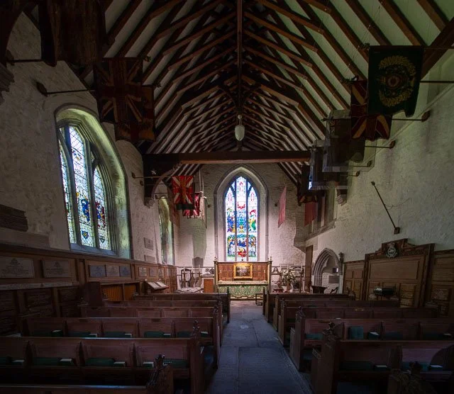 Interior of a church with wooden pews, stained glass windows, and a central altar with colorful stained glass backdrop.